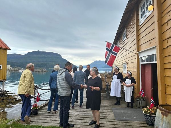Gjester på trebrygga med norsk flagg, bunad og fjordutsikt