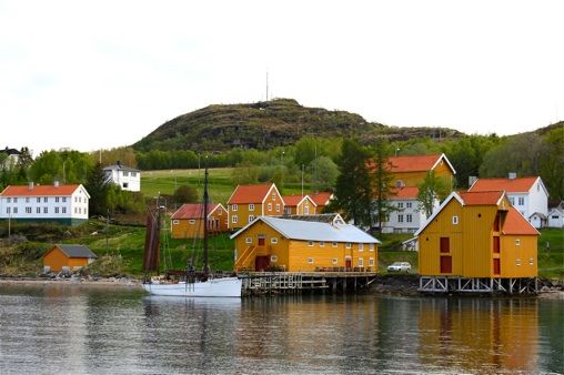 Hamnvik Handelssted sett fra sjøen, med gule sjøhus langs brygga