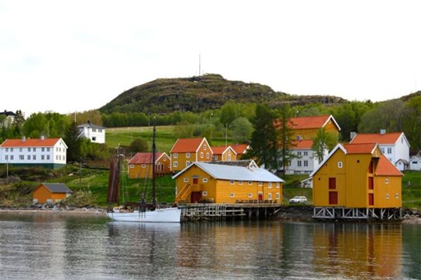 Hamnvik Handelssted sett fra sjøen, med gule sjøhus langs brygga