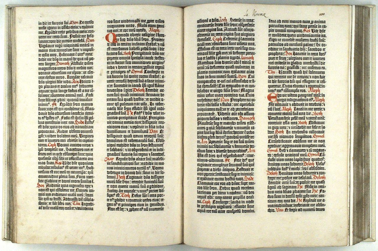 An open ancient book with two pages visible, showing dense Latin text, red rubrication, and large illuminated initials.