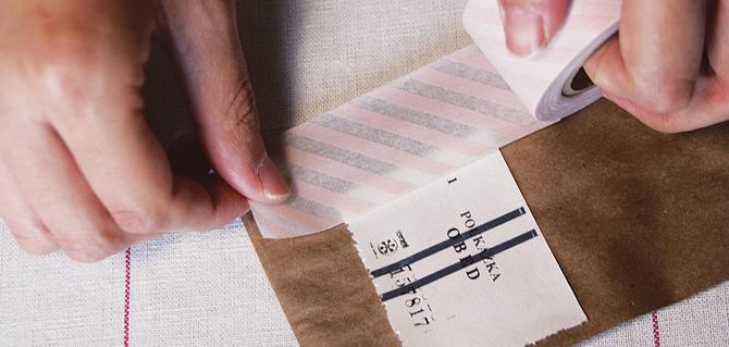 Hands applying a piece of washi tape with transparent pink stripes to a label