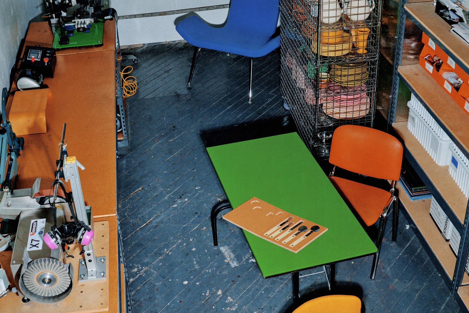 Workshop room with colorful chairs, green table, utensils sample board, shelving, and tools scattered around.