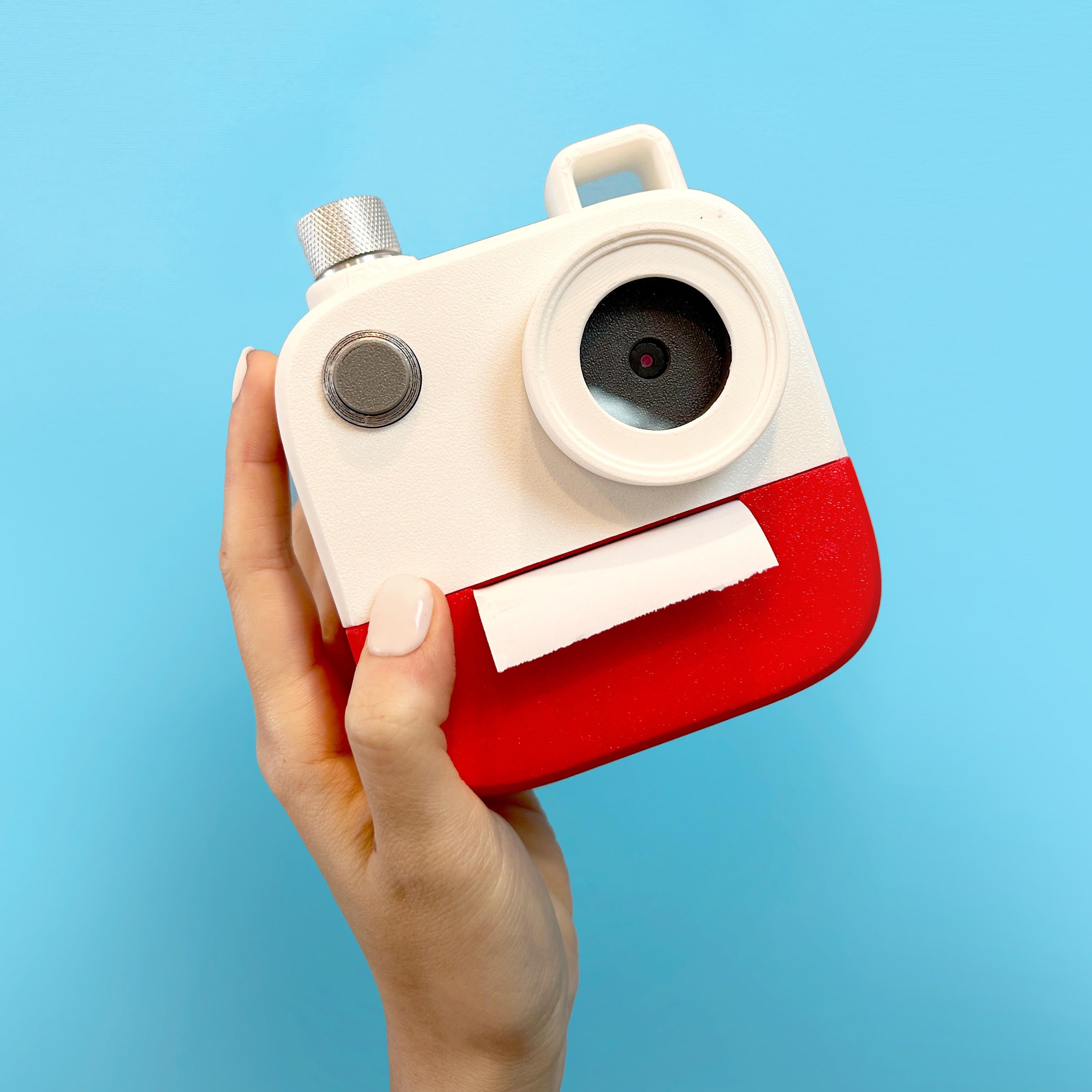 A hand with painted nails holds a whimsical red and white toy camera against a bright blue background.
