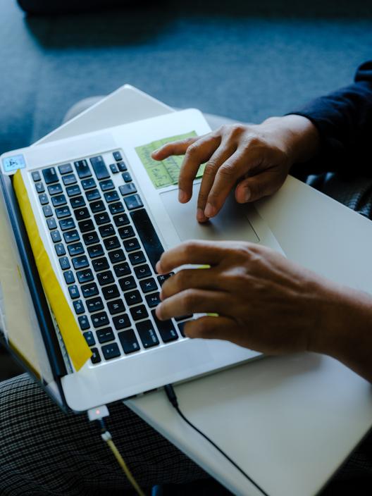 A fellow’s hands type on the keyboard of an Apple laptop