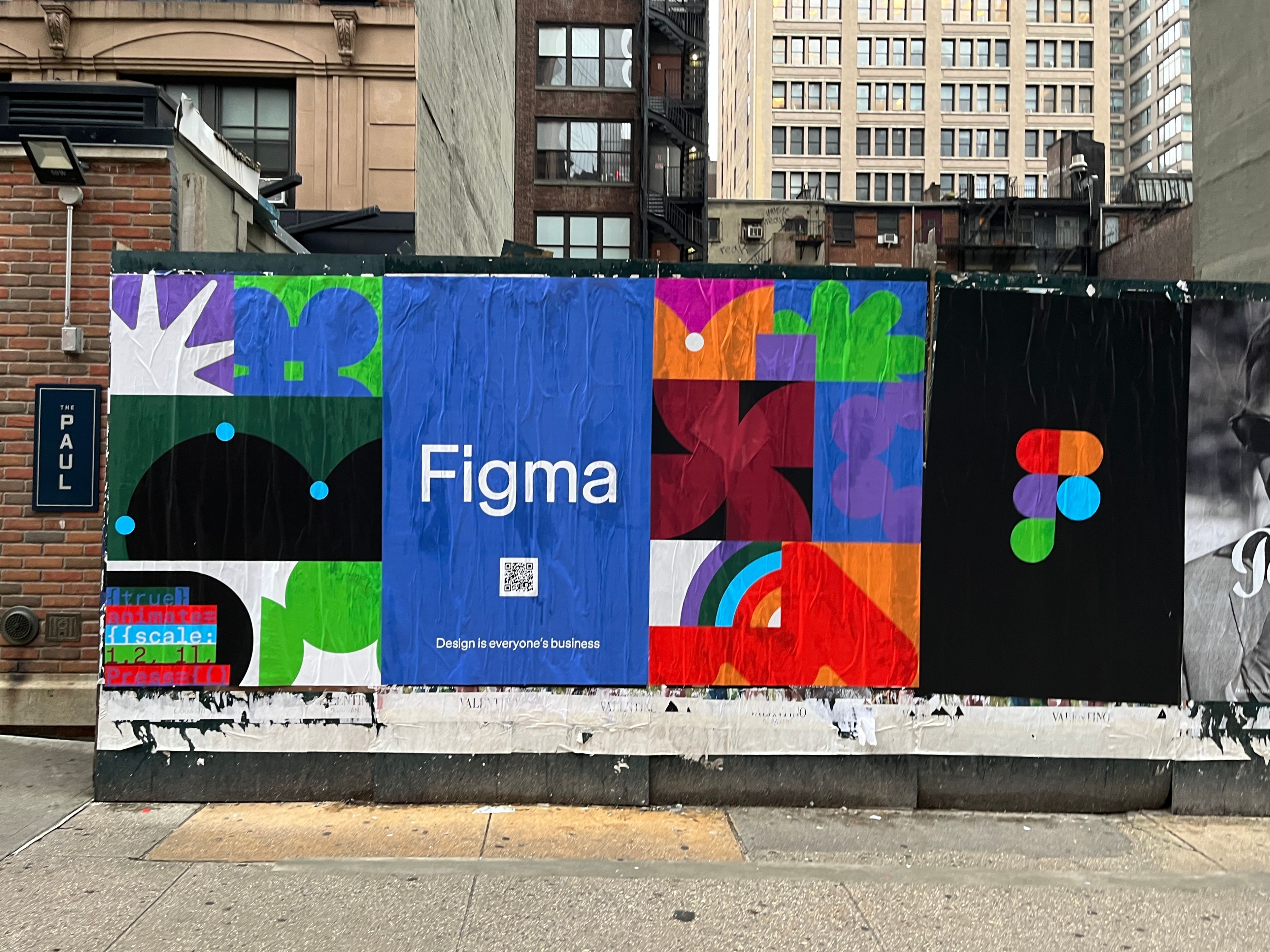 A wildposting wall featuring multiple colorful Figma posters, including the logo, geometric shapes, and the phrase “Design is everyone’s business,” pasted along a city sidewalk.