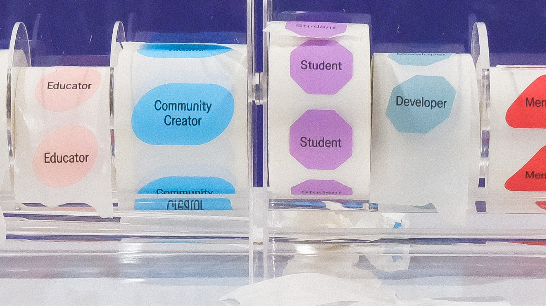 Colorful sticker rolls labeled “Educator,” “Community Creator,” “Student,” “Developer,” and “Mentor” displayed in plastic dispenser
