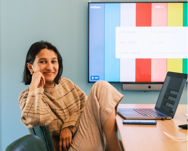 A Figmate smiling at the camera with a laptop on a table