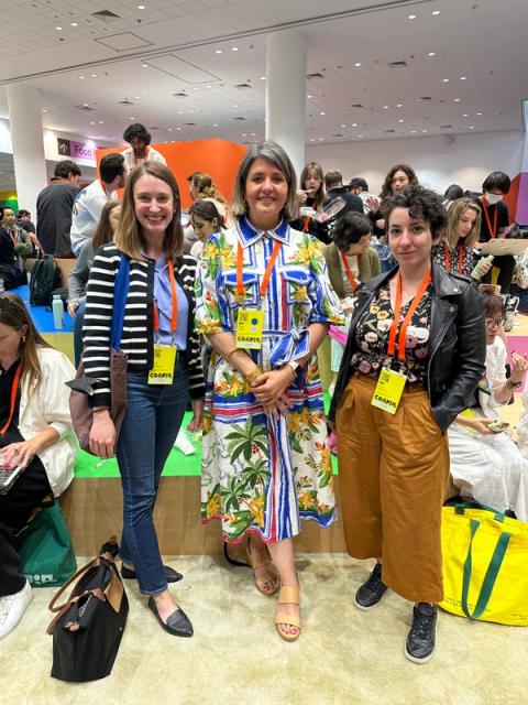 Three woman stand, showing off outfit highlights like a tropical patterned button-down dress and a leather jacket over tan culottes