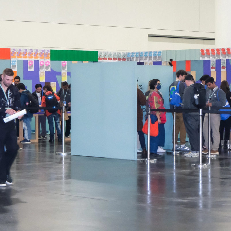 People gather and read printed poster sheets displayed on colorful walls inside a Config event space.