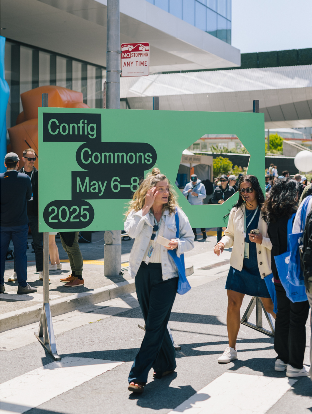 Attendees walk past green Config Commons sign displaying event dates: May 6–8, 2025.