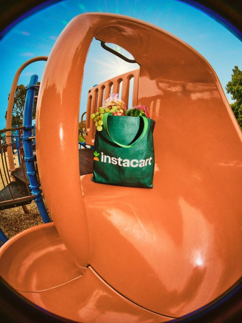 Green Instacart tote filled with fresh produce sits on the top of an orange slide