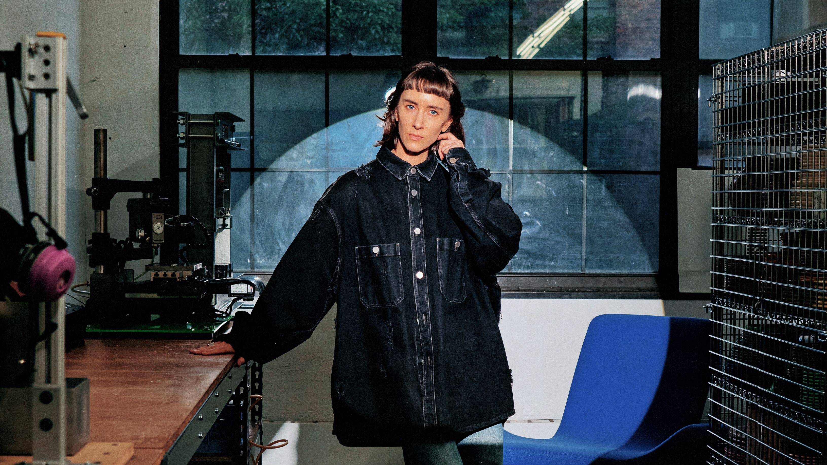 Photograph of a woman in an oversize jacket in an industrial studio, illuminated by a bright spotlight.