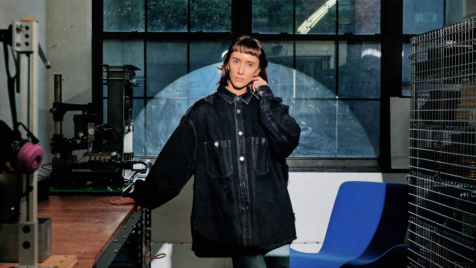 Photograph of a woman in an oversize jacket in an industrial studio, illuminated by a bright spotlight.