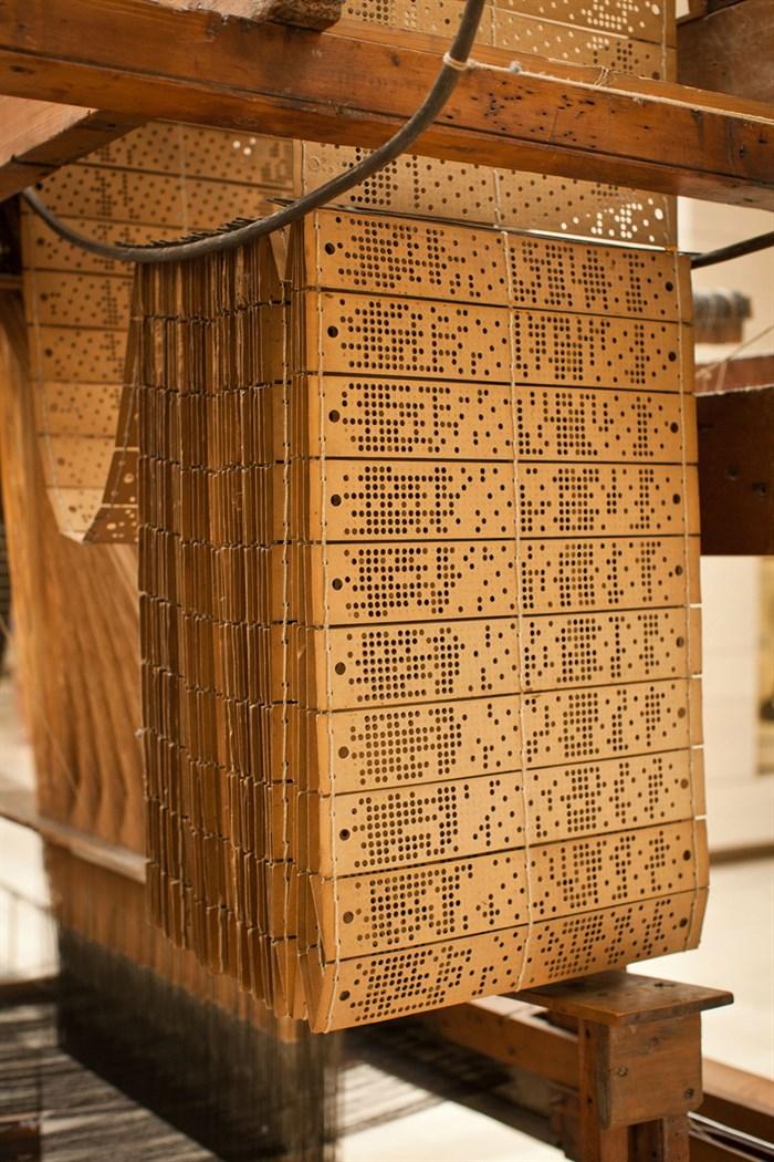 Wooden cards with various perforations sewn together and hanging from a loom