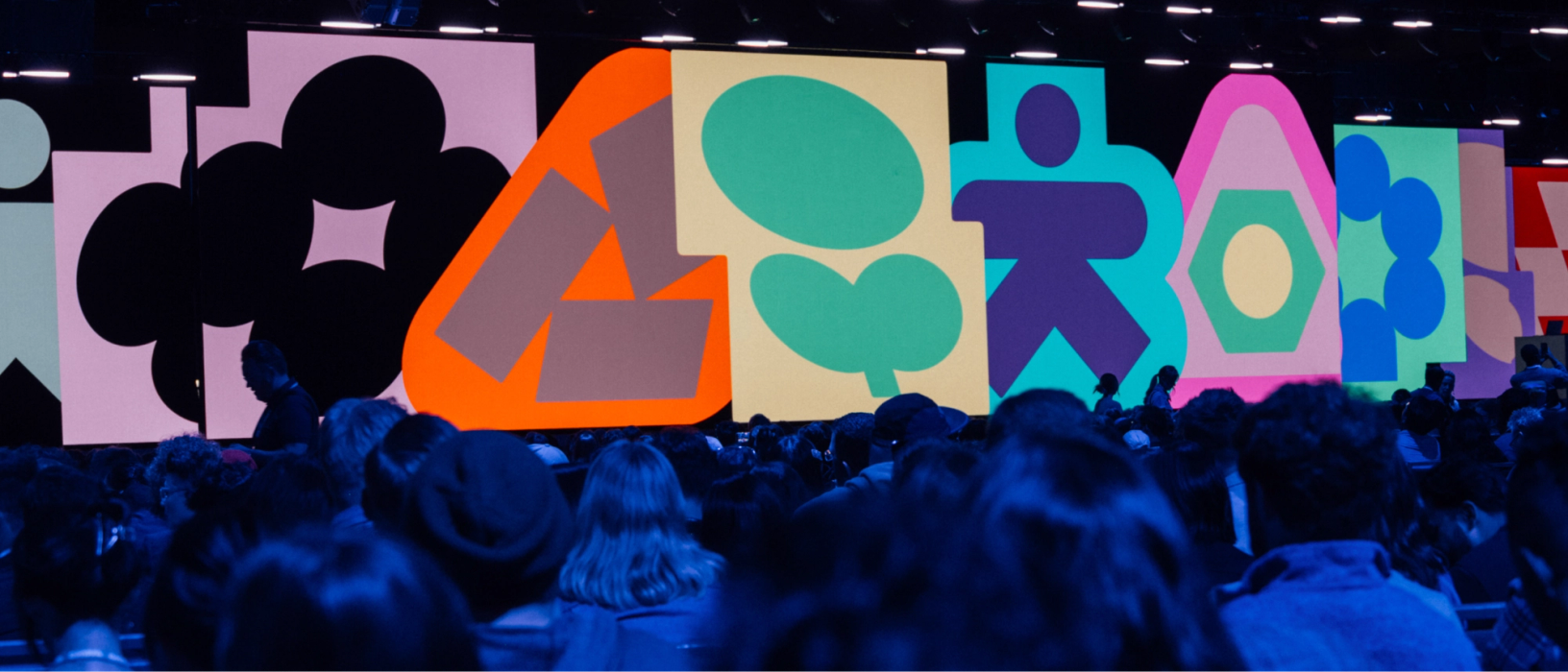 Audience gathers in darkened keynote hall, facing vibrant Config icon visuals on massive stage screen.
