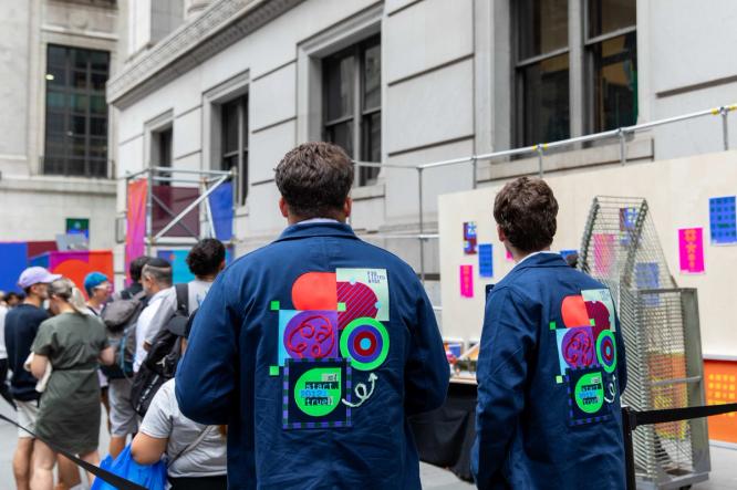Two team members in custom Figma jackets walk past a busy event booth.