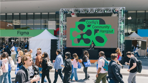 Crowd passes outdoor stage with “Config’s Community Hangout” screen as DJ performs near Figma venue.
