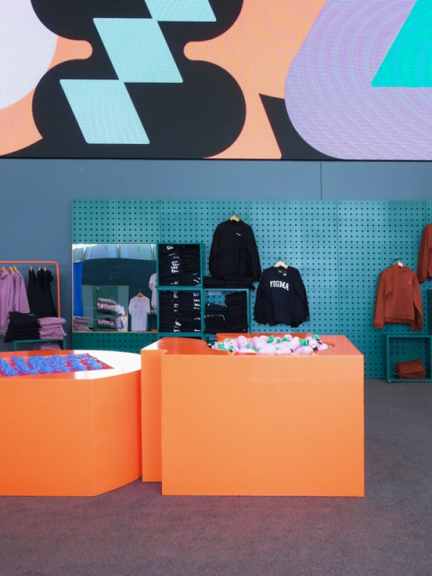 Merchandise and plush toys displayed in The Figma Store with large screen showcasing Config designs.