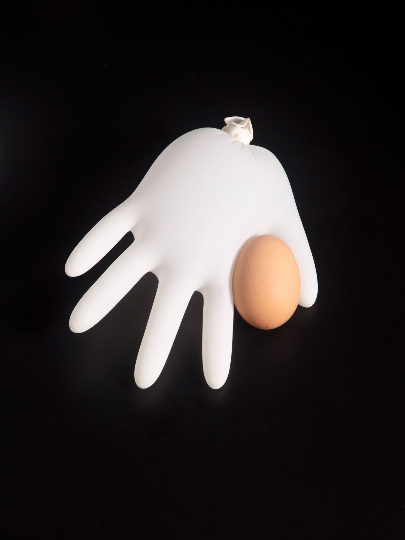 Inflated white glove beside a brown egg on a black background.