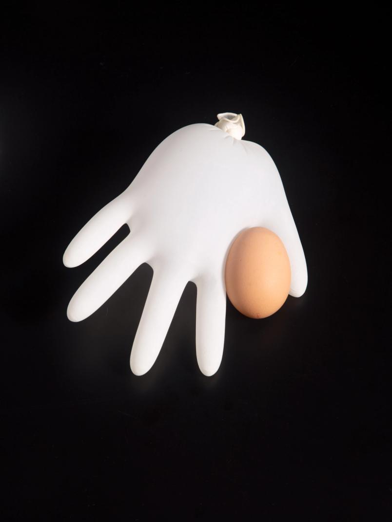 Inflated white glove beside a brown egg on a black background.