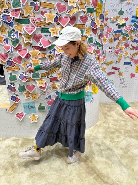 A woman poses with her arms out. She's wearing a houndstooth cardigan, a tiered blue maxi skirt, and a white cap