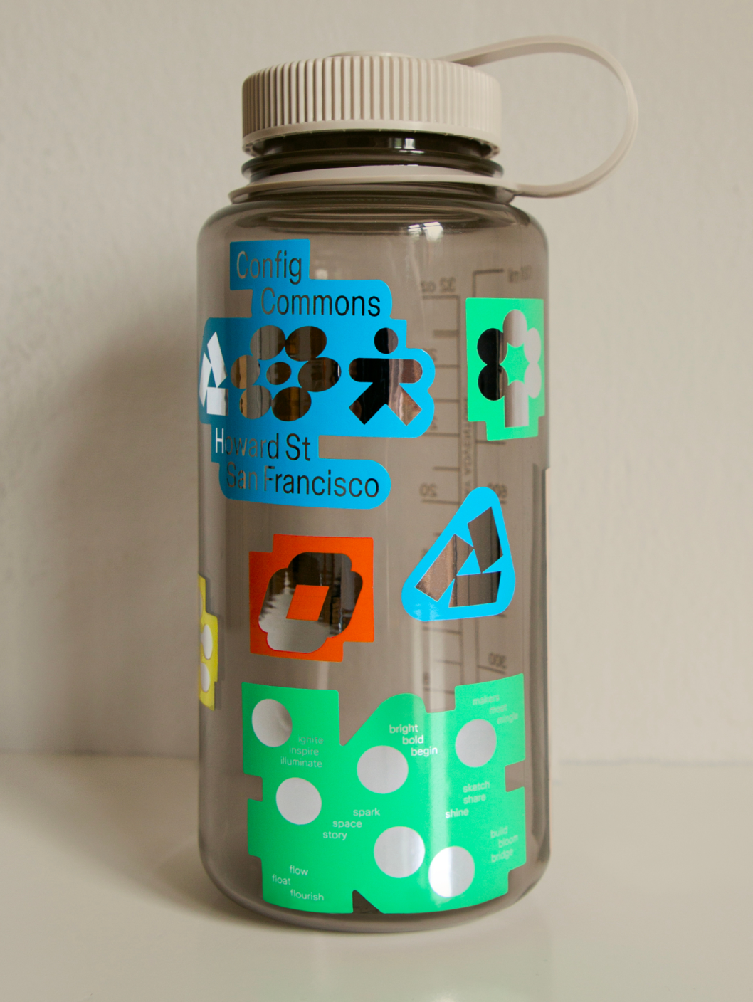 Clear Nalgene bottle decorated with colorful Config Commons icons and inspirational words like “spark” and “shine.”