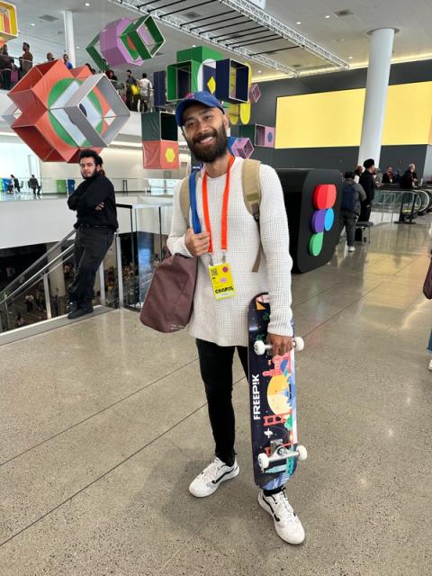 A man wears a textured white long sleeve tee and carries a skateboard