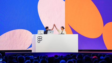 Two presenters high-five onstage at Figma conference, colorful abstract shapes fill the large background screen.