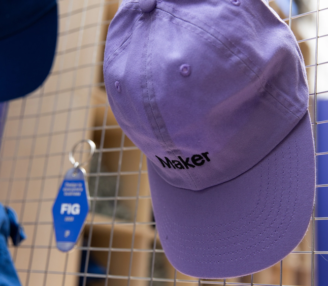 A lavender “Maker” hat hangs on a merch wall display.