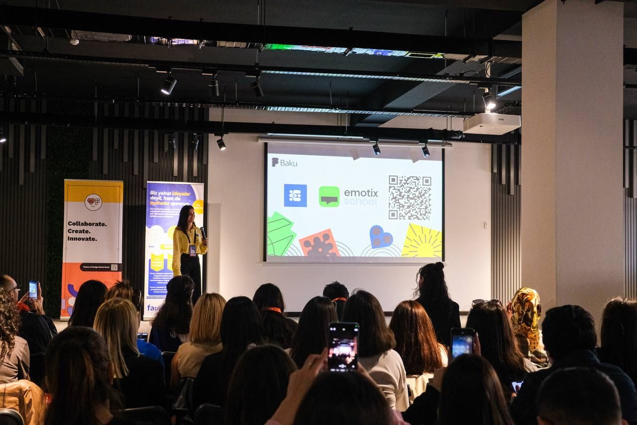 Individual speaks on stage in front of audience next to presentation