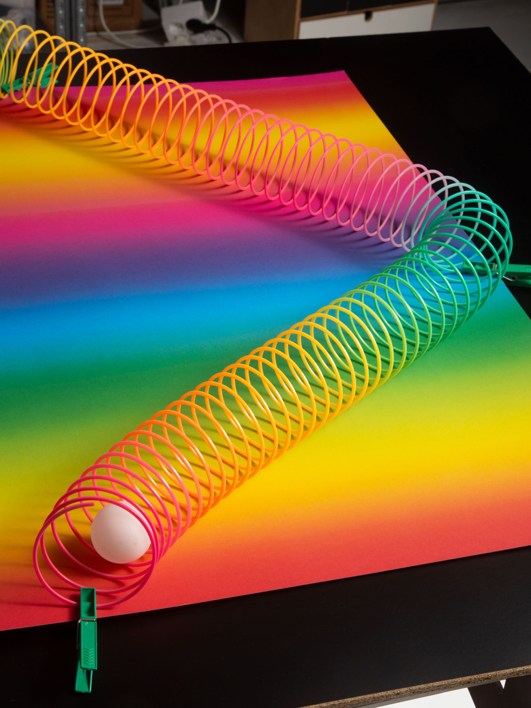 Rainbow-colored plastic slinky stretched across a vibrant gradient sheet with an egg inside one end.