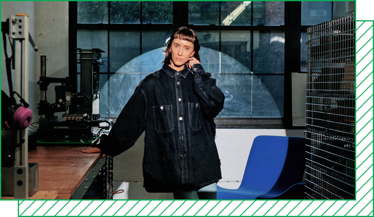 Photograph of a woman in an oversize jacket in an industrial studio, illuminated by a bright spotlight.