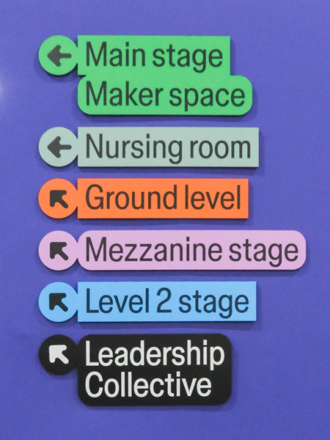 Color-coded event signs with arrows point to stages, nursing room, and Leadership Collective at venue.