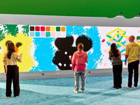 Attendees paint with a giant digital canvas and pen-shaped controller, adding colorful shapes to a shared mural