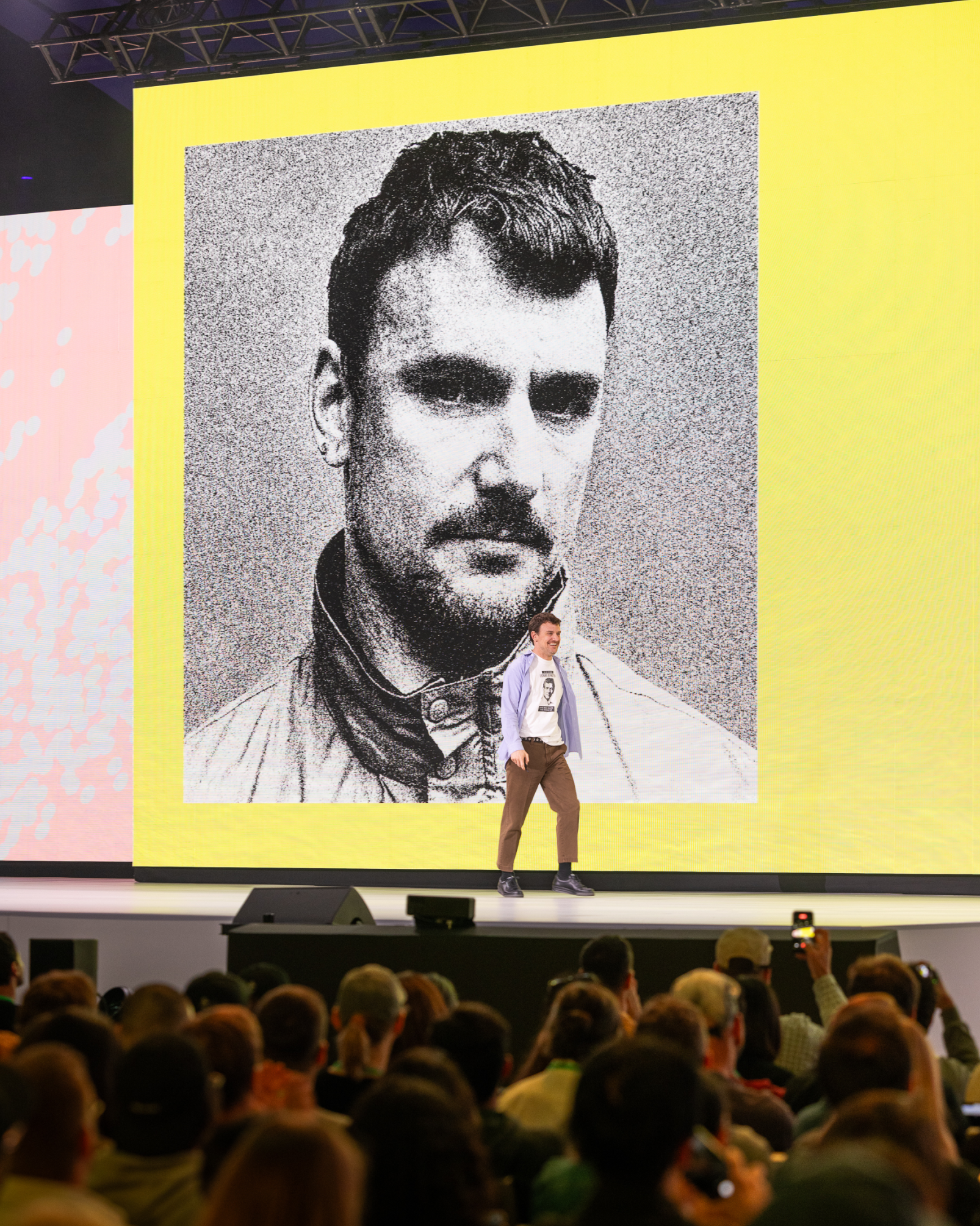 A speaker walks onstage with his black-and-white headshot displayed behind him.