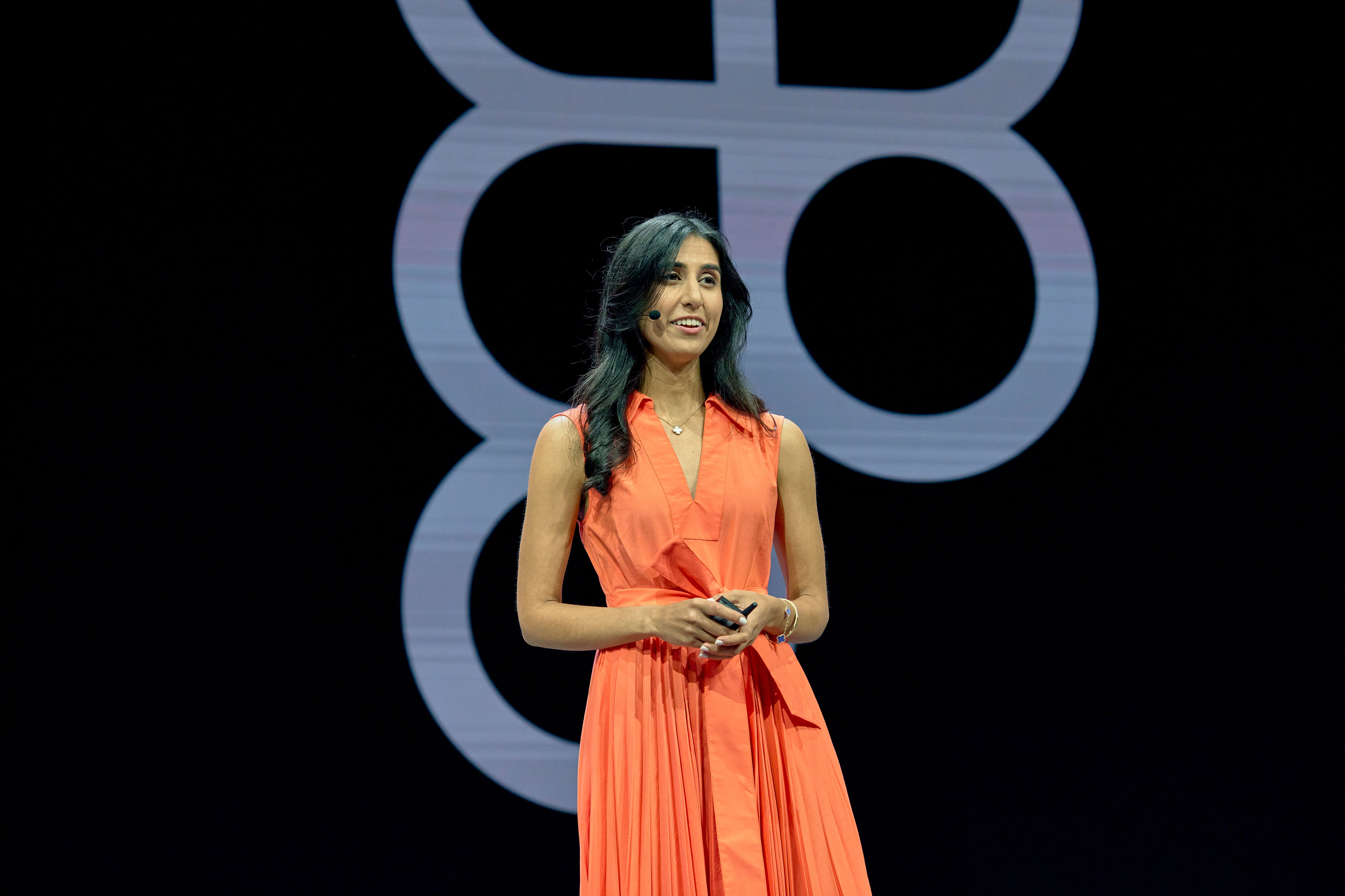 A woman in a bright orange dress stands on stage with the Figma logo in the background