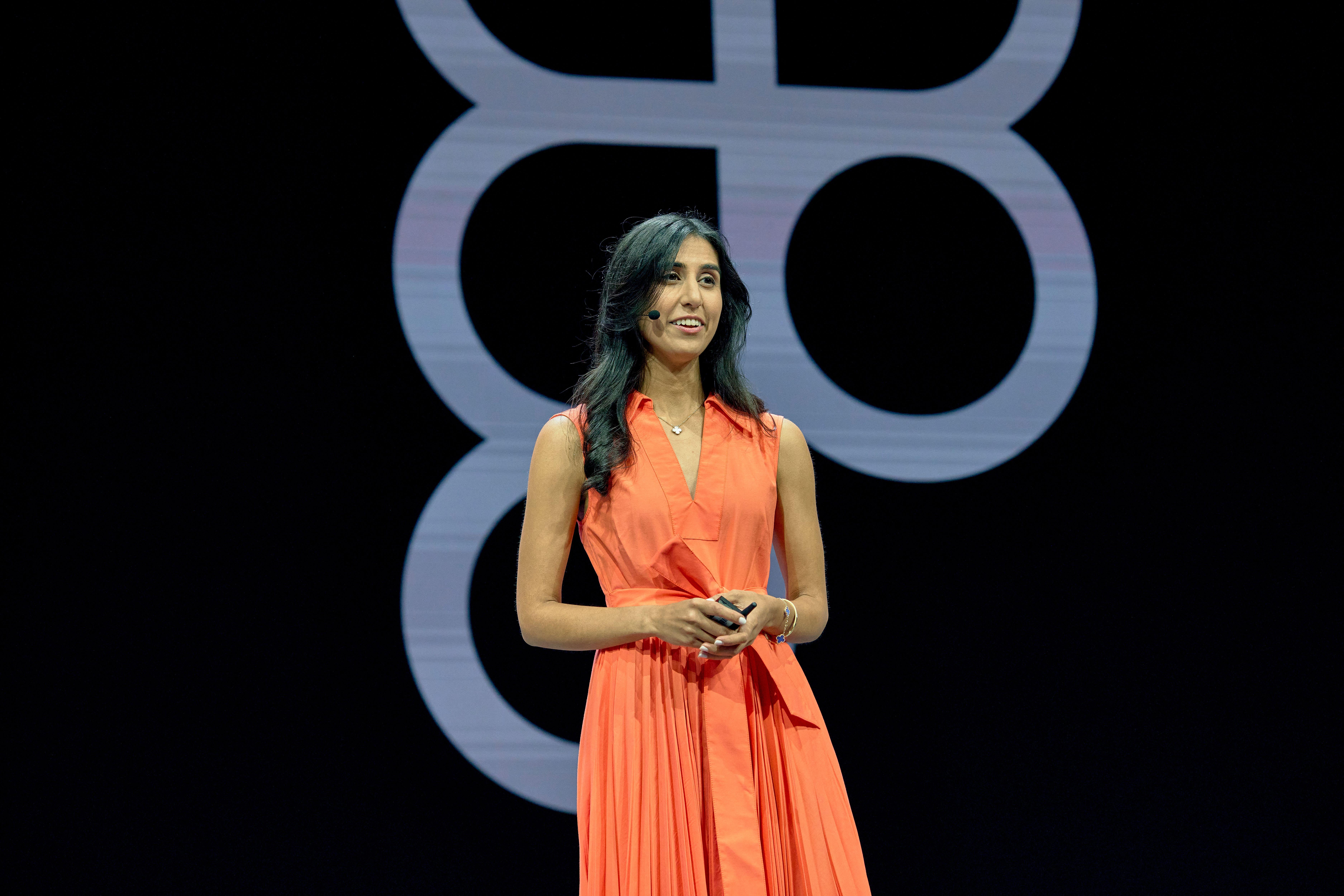 A woman in a bright orange dress stands on stage with the Figma logo in the background