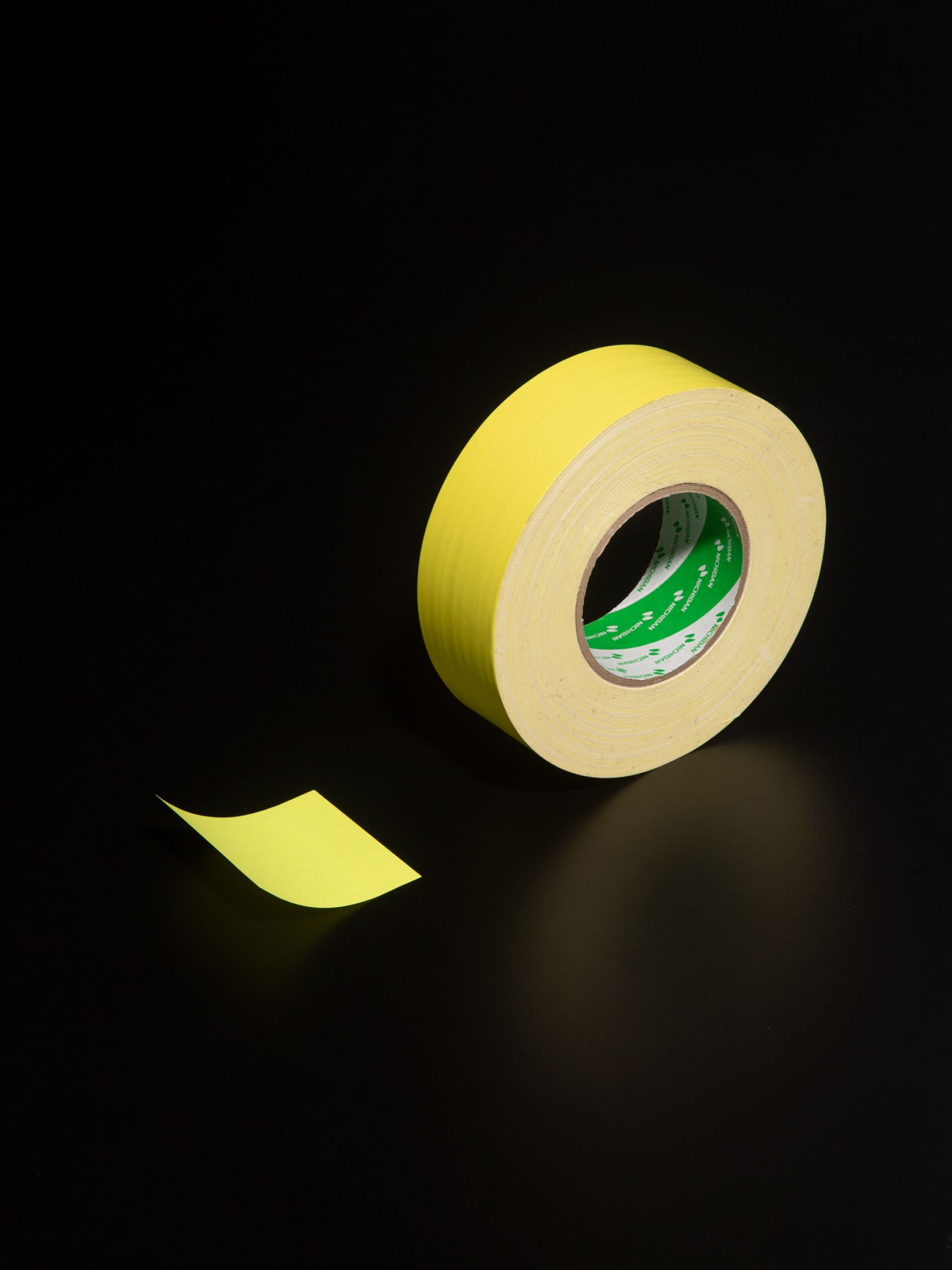 Yellow masking tape roll with a peeled strip resting on a black surface.