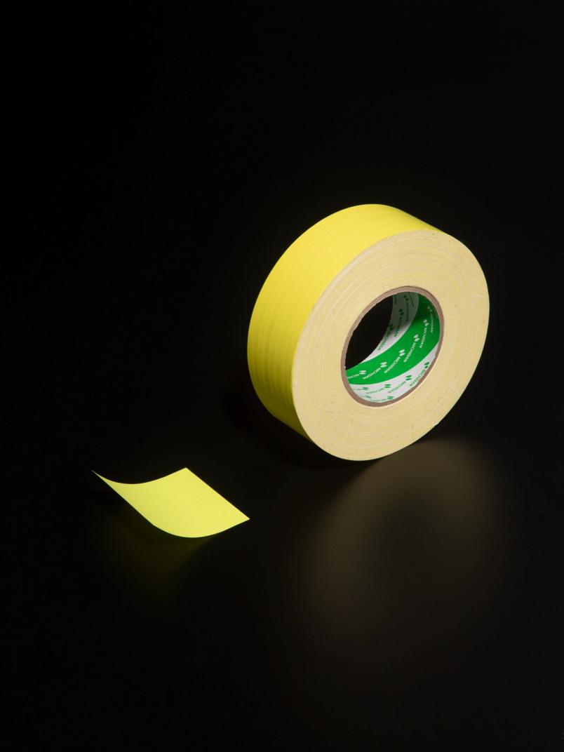 Yellow masking tape roll with a peeled strip resting on a black surface.