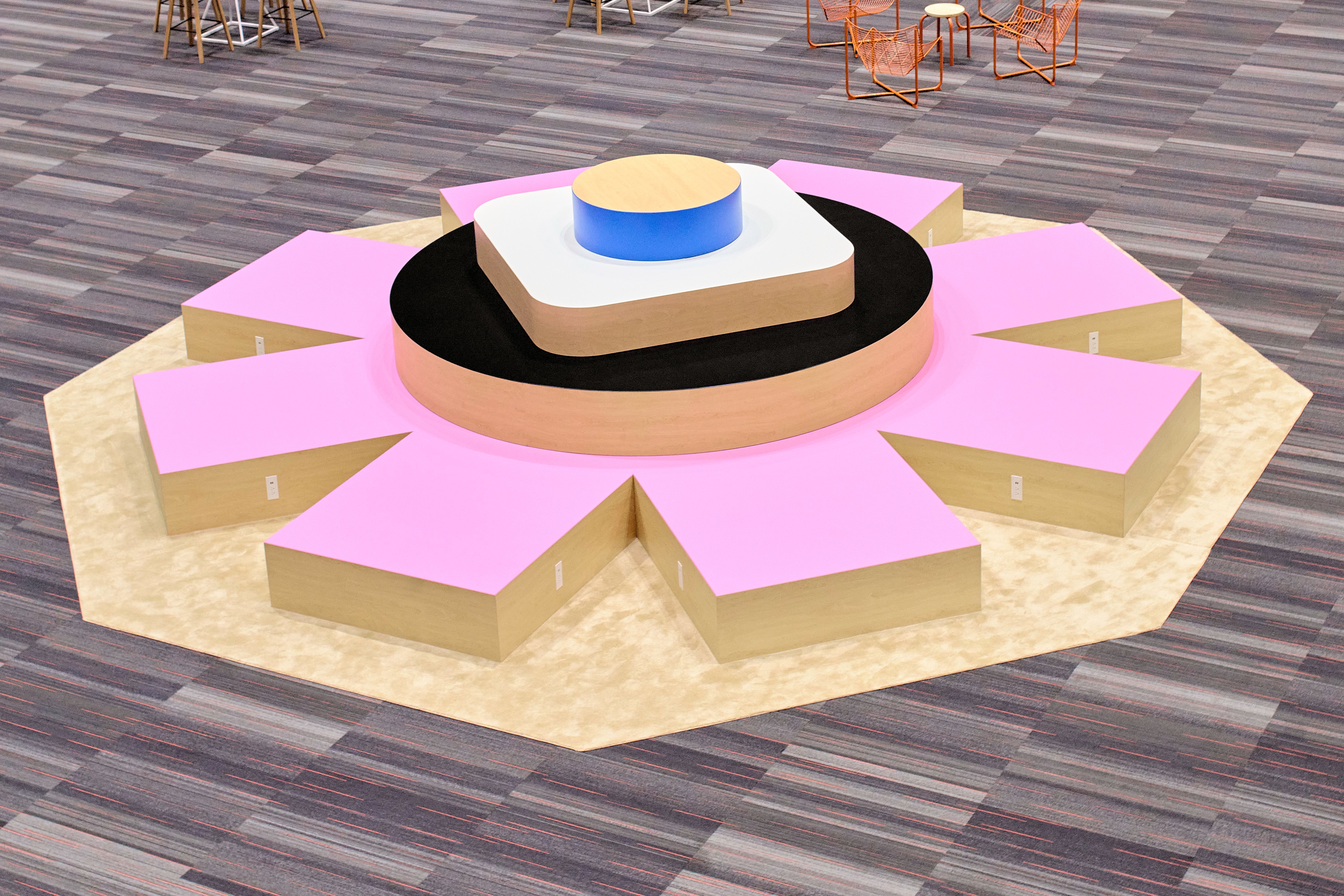 An aerial image of a large pink asterisk structure, with smaller circle and square shapes on top. There are neighboring chairs surrounding the structure, showing that comparatively, this asterisk structure is high enough for seating. 