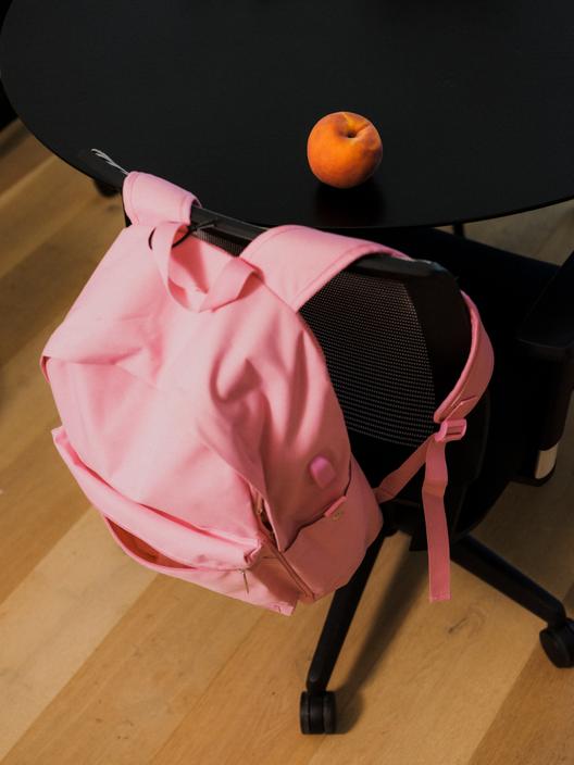 A pink backpack hangs on a rolling chair, and a peach rests on a desk