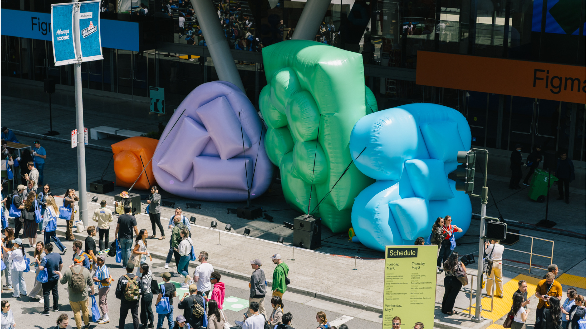 Large colorful inflatables line sidewalk outside Config entrance as attendees gather under sunny sky.
