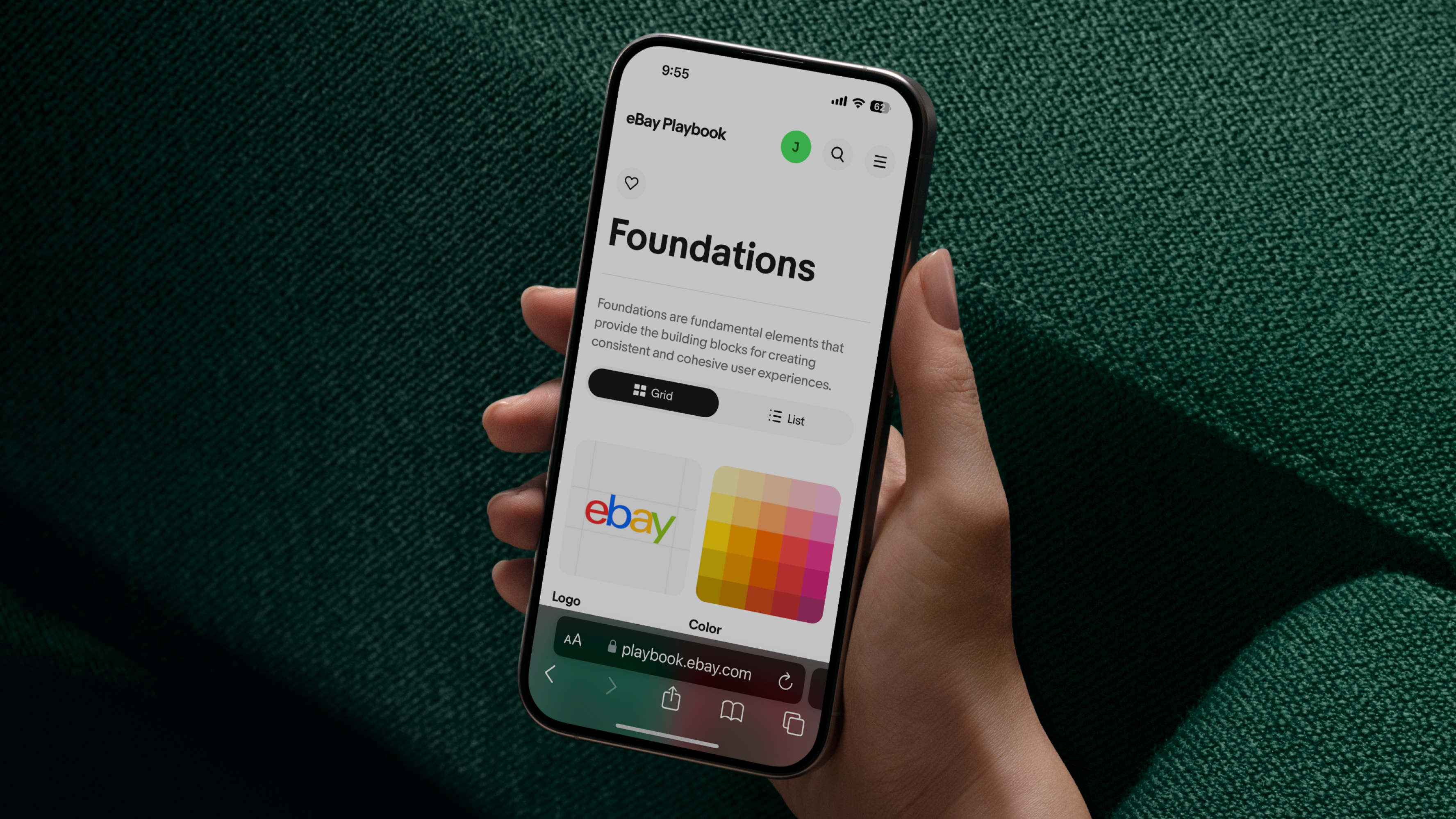 A hand holding a smartphone displaying the "eBay Playbook" design system on a dark green fabric background. The screen shows the "Foundations" section with options for grid or list views and colorful tiles representing logo and color guidelines.