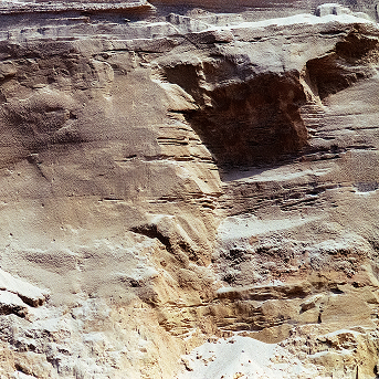 A close-up photograph of a layered sandstone rock face with warm ochre and cream tones.