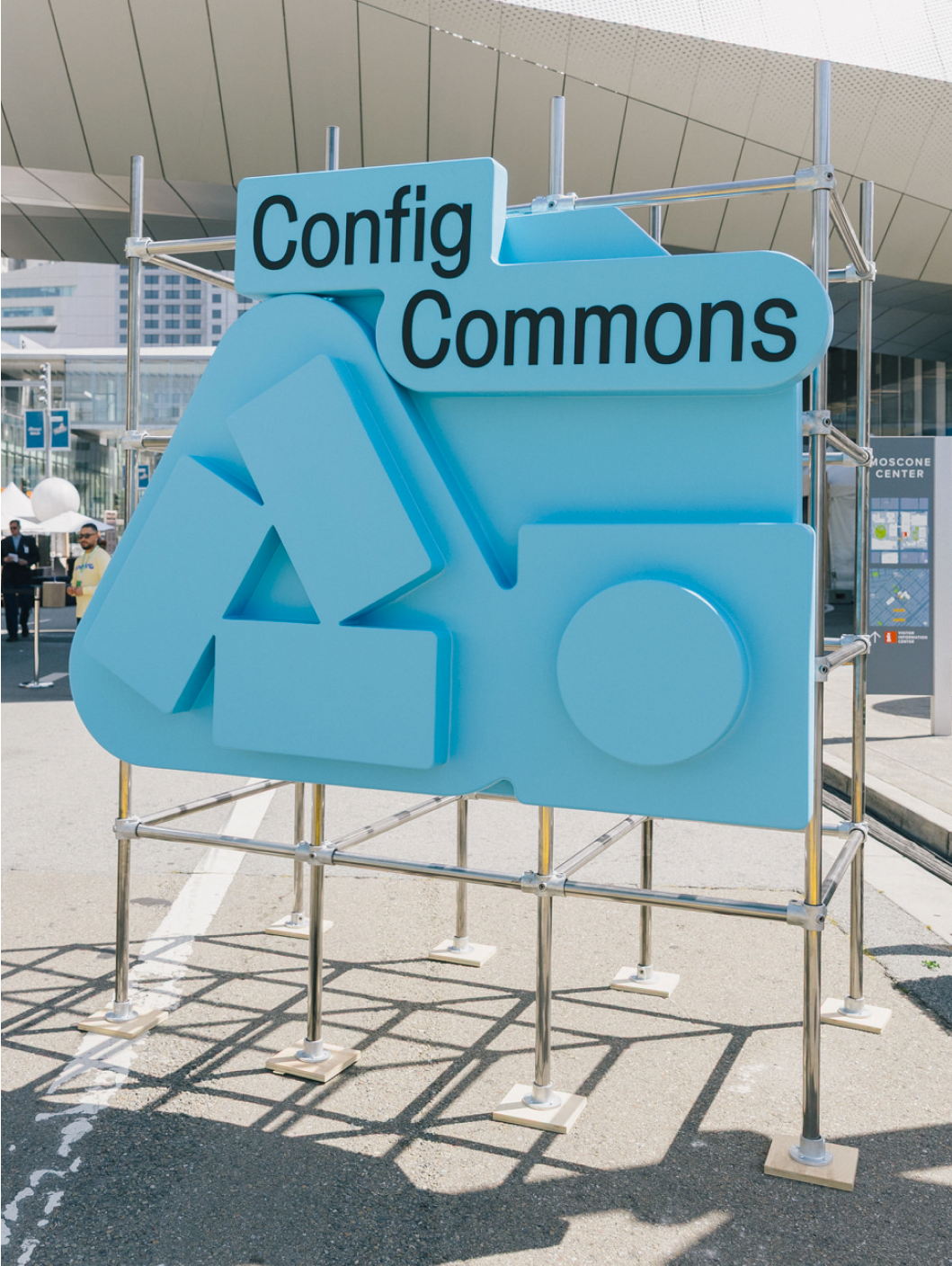 Large blue “Config Commons” sculpture with abstract icons stands on scaffolding near Moscone Center entrance.