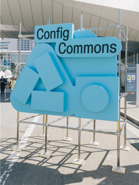 Large blue “Config Commons” sculpture with abstract icons stands on scaffolding near Moscone Center entrance.