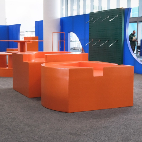 Glossy orange modular furniture shaped like Config icons stands in front of blue divider walls