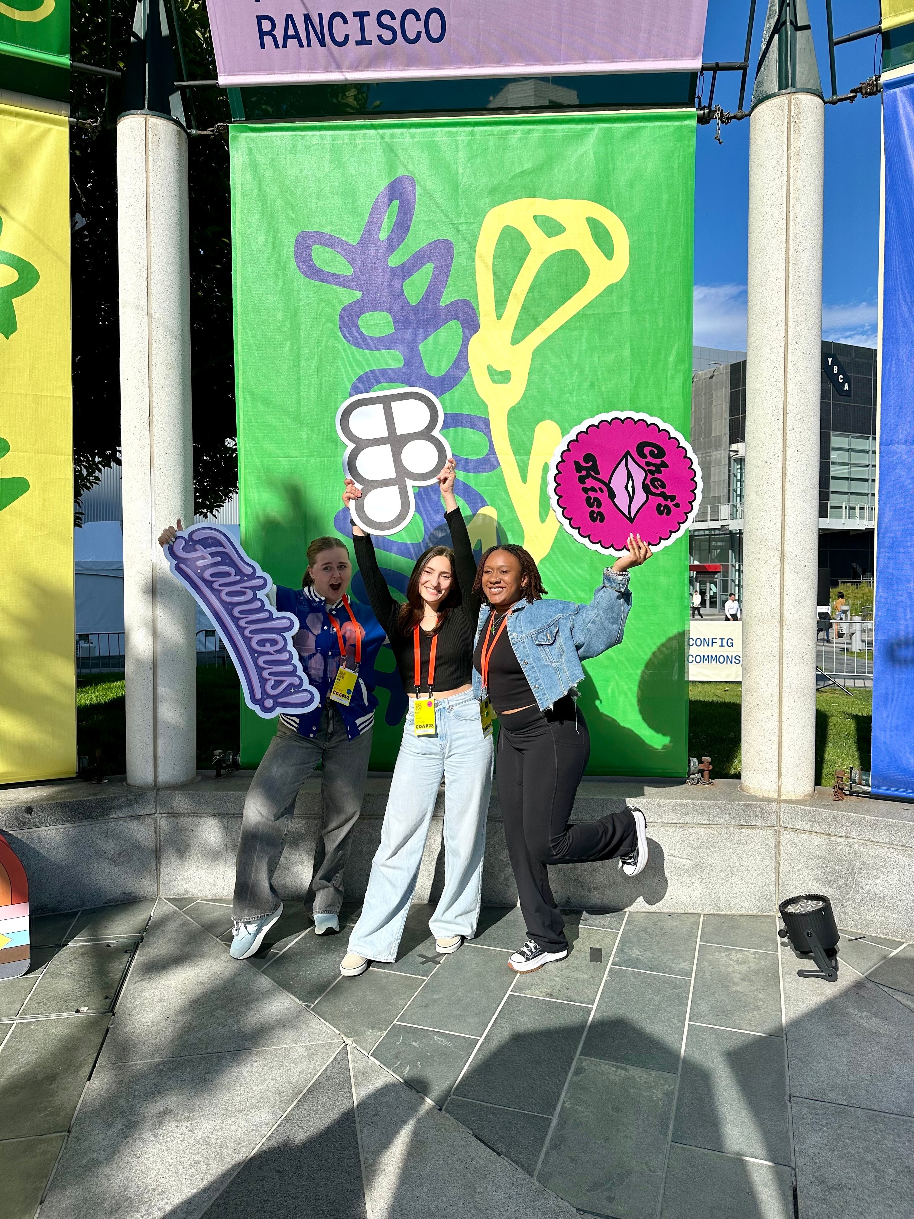 Three friends pose with Figma-related props in front of an abstract green backdrop.