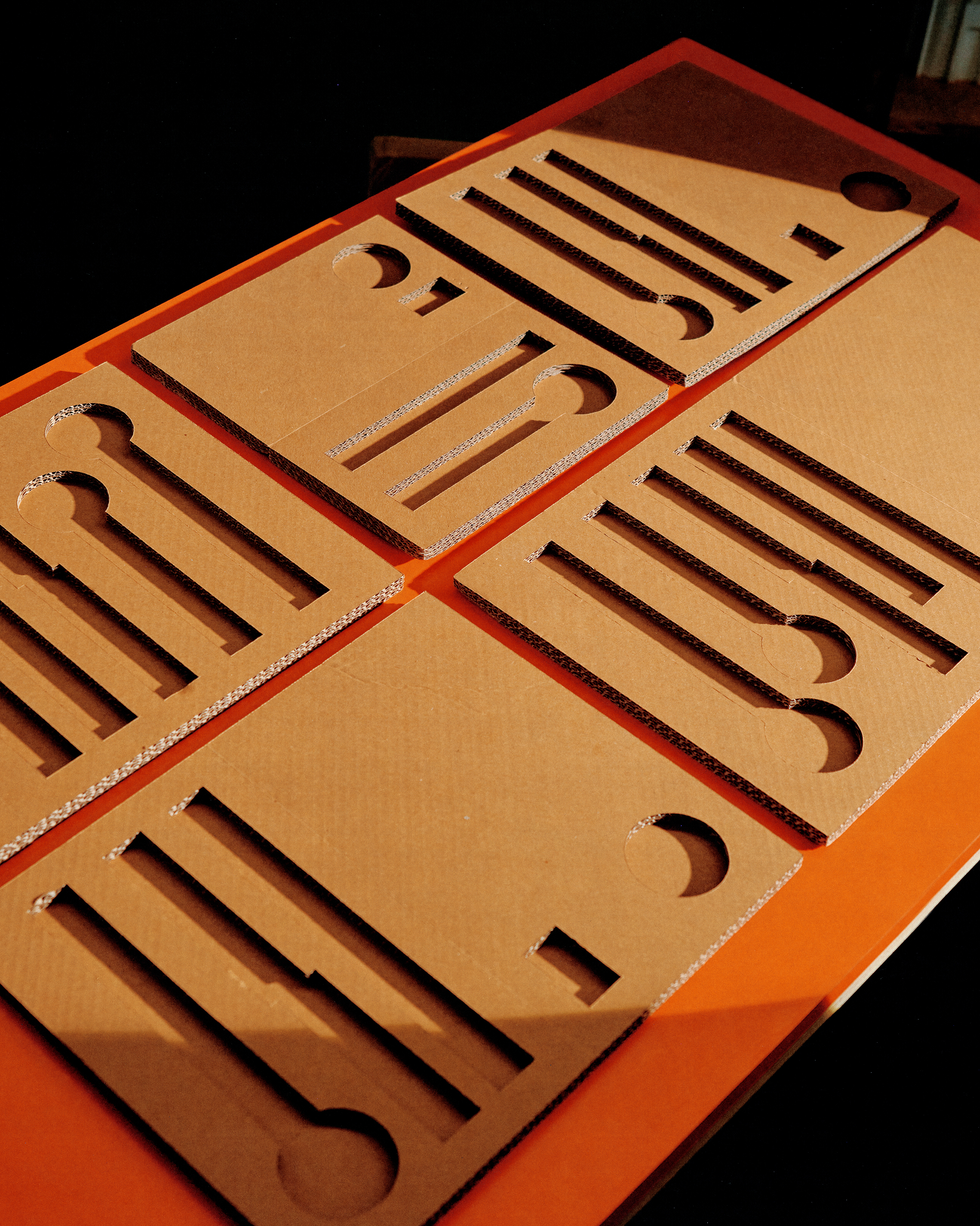  Cardboard sheets with precisely cut utensil-shaped slots arranged on orange surface under angled warm light.