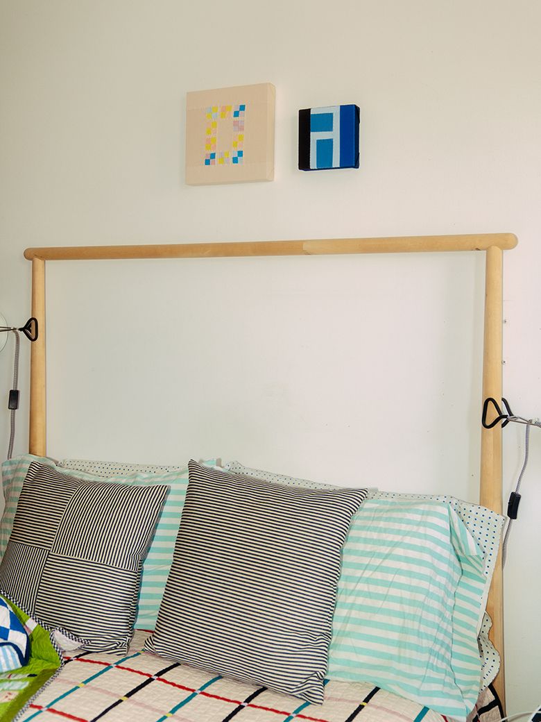 A photograph of the grid quilt on Nicole’s bed, which has two small quilt blocks hanging above a wooden headboard.